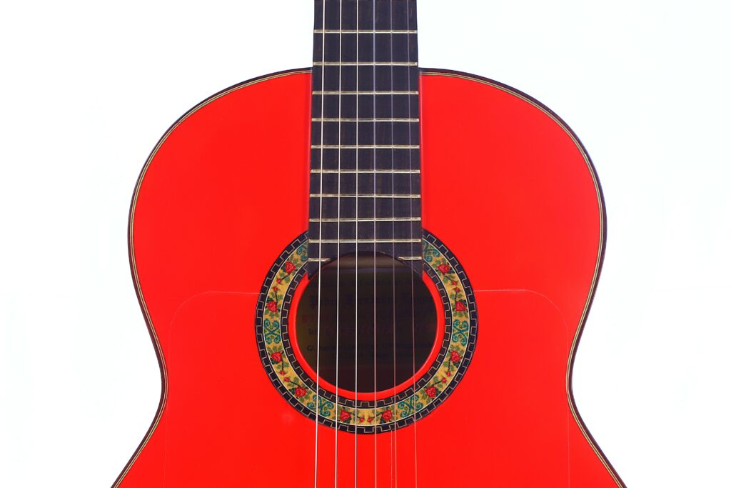 A Close-Up Of The Pedro Fernández Luque 2021 Blanca Flamenco Guitar Highlights Its Bright Red Body, Decorative Rosette Around The Sound Hole, And Lower Fretboard, All Set Against A White Background.