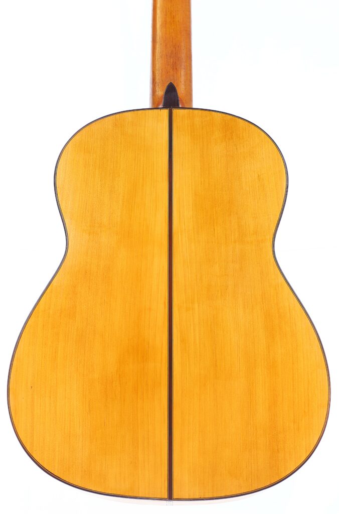 The Image Displays The Back Of The Gerundino Fernandez 1990 Flamenco Guitar, Featuring A Light Wood Finish, A Dark Center Seam, Smooth Rounded Edges, And An Extended Neck At The Top.