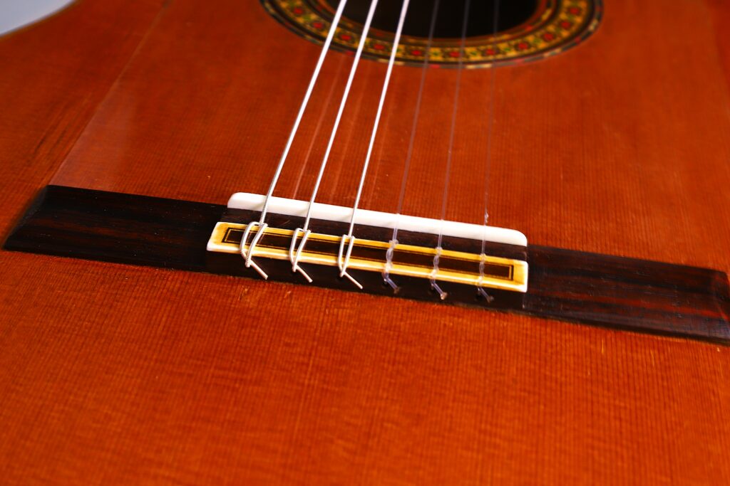 Close-Up Of The Gerundino Fernandez 1990 Flamenco Guitar Bridge And Strings, Highlighting The Wood Grain, Bridge, And A Portion Of The Sound Hole With Its Decorative Rosette.