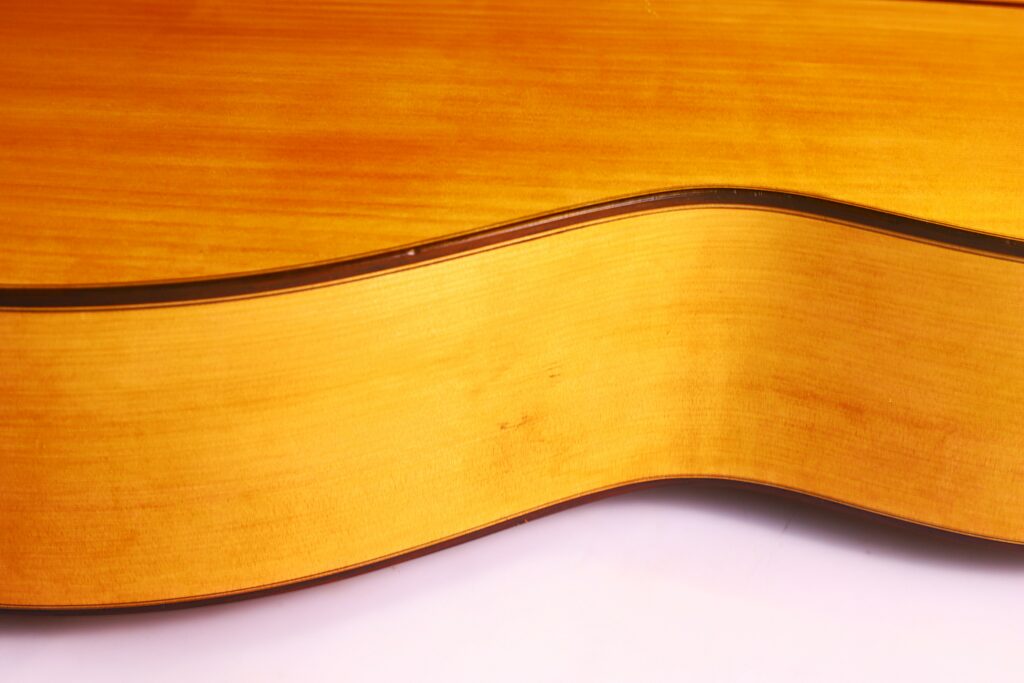 Close-Up Of The Gerundino Fernandez 1990 Flamenco Guitar’s Side, Highlighting Its Curved Wooden Body With A Warm Amber Finish Set Against A White Background.