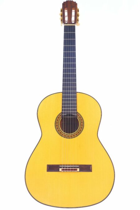 The Manuel Reyes 1991 Flamenco Guitar features a yellowish wooden body, dark fretboard, and an intricate rosette around the sound hole, displayed against a plain white background.