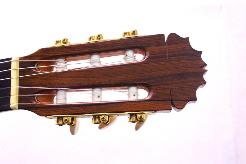 Nahaufnahme Der Kopfplatte Einer Manuel Reyes 1991 Flamenco-Gitarre Mit Holzfinish, Goldenen Stimmwirbeln Und Weißen Stimmpfosten Vor Einem Schlichten Weißen Hintergrund.