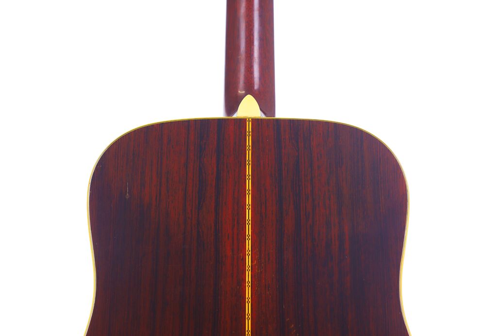 Nahaufnahme Der Rückseite Einer Martin D-28 1950 Akustik Gitarre, Die Ihre Glänzende Dunkle Holzoberfläche Mit Einer Zentralen Vertikalen Ziereinlage Und Gelben Einfassungen Entlang Der Kanten Hervorhebt.