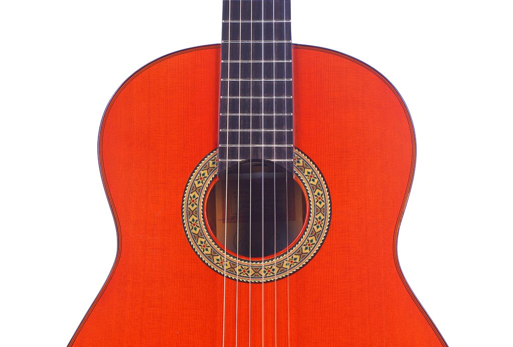Nahaufnahme Der Hermanos Conde 1991 Paco De Lucia Special Flamenco Gitarre, Die Ihre Leuchtend Orangefarbene Lackierung, Die Dekorative Schalllochrosette Und Sechs Saiten Vor Einem Weißen Hintergrund Zeigt.