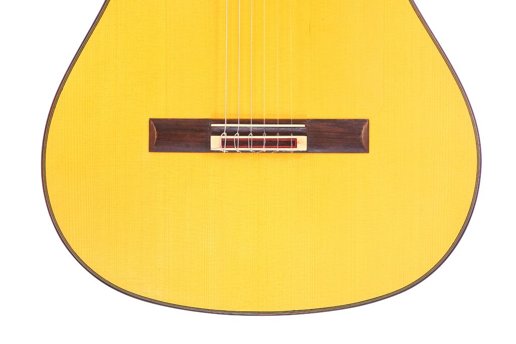 Nahaufnahme Der Unteren Hälfte Einer Manuel Reyes Flamenco-Gitarre Aus Dem Jahr 1991, Die Den Gelben Holzkorpus, Die Saiten Und Den Dunklen Holzsteg Hervorhebt.