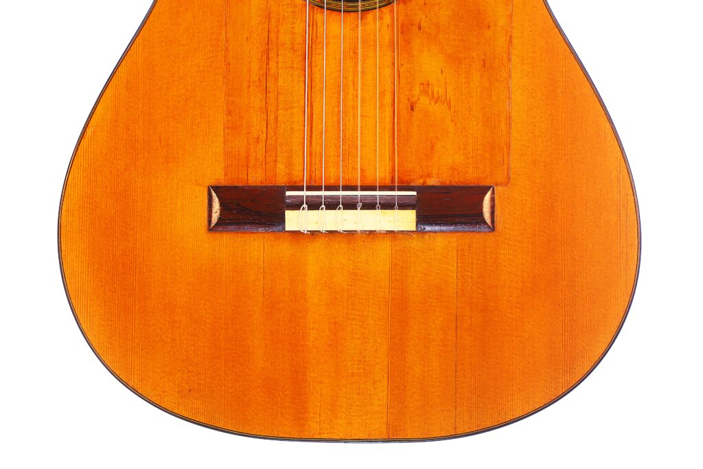 Santos Hernandez 1930 年弗拉门戈吉他琴身特写,配有六根弦、木制琴桥和橙棕色亮面漆。看不到琴颈和琴头。.