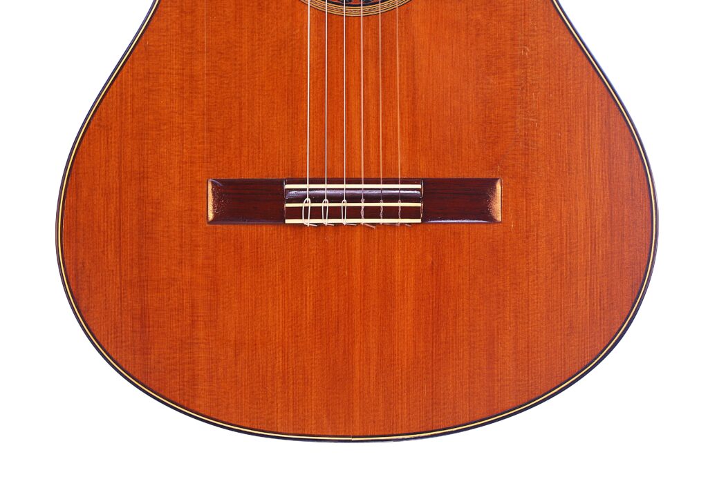 Nahaufnahme Der Manuel Reyes Model 2021 Von Hippner Flamenco Gitarre, Die Ihre Holzoberfläche, Saiten Und Den Steg Mit Einem Warmen Braunen Finish Und Detaillierter Holzmaserung Hervorhebt.