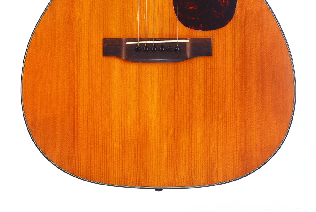 Nahaufnahme Des Korpus Der Martin 000-18 1958 Akustik Gitarre, Die Ihre Holzmaserung, Saiten, Den Steg Und Einen Teil Des Schlagbretts Vor Weißem Hintergrund Hervorhebt.