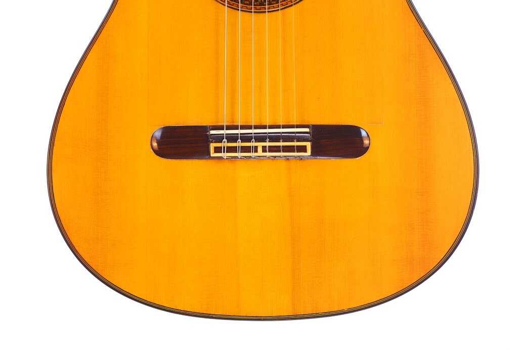 Nahaufnahme Der Unteren Hälfte Einer Luis Sanchez 2011 Negra Flamenco Gitarre, Die Die Saiten, Den Steg Und Die Warme Holzoberfläche Des Instruments Detailliert Zeigt.