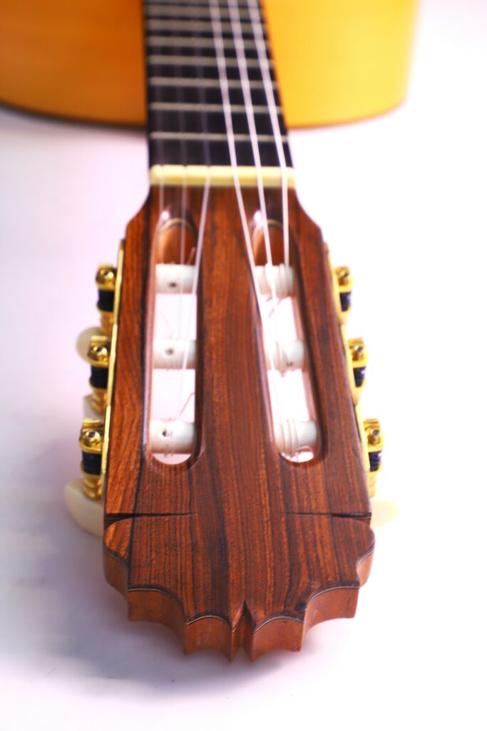 Nahaufnahme Der Kopfplatte Einer Manuel Reyes Flamenco-Gitarre Aus Dem Jahr 1991 Mit Holzfinish, Weißen Stimmwirbeln Und Goldenen Mechaniken, Wobei Im Hintergrund Der Hals Und Ein Teil Des Korpus Zu Sehen Sind.