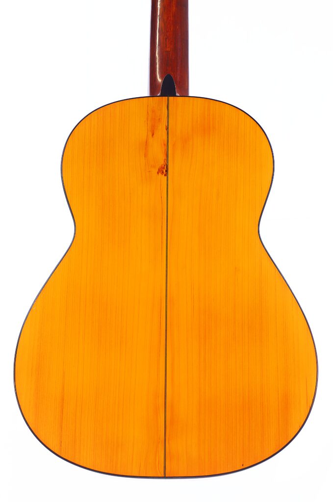 图片显示的是 Santos Hernandez 1930 弗拉门戈吉他的背面,木质表面呈浅棕色,富有光泽,中间有一条垂直的黑色接缝。顶部可以看到吉他的部分琴颈。.