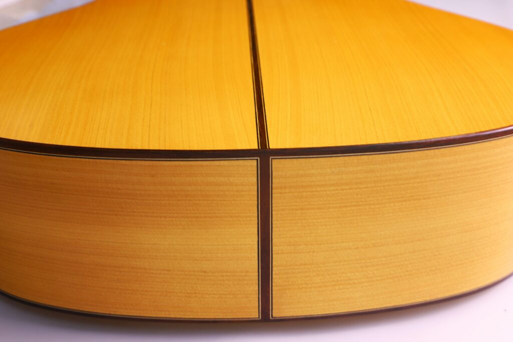 Nahaufnahme Des Bodens Und Der Zargen Einer Manuel Reyes Flamenco-Gitarre Aus Dem Jahr 1991 Mit Glattem, Hellgelbem Holz, Dunklen Verzierungen Und Klaren Linien.