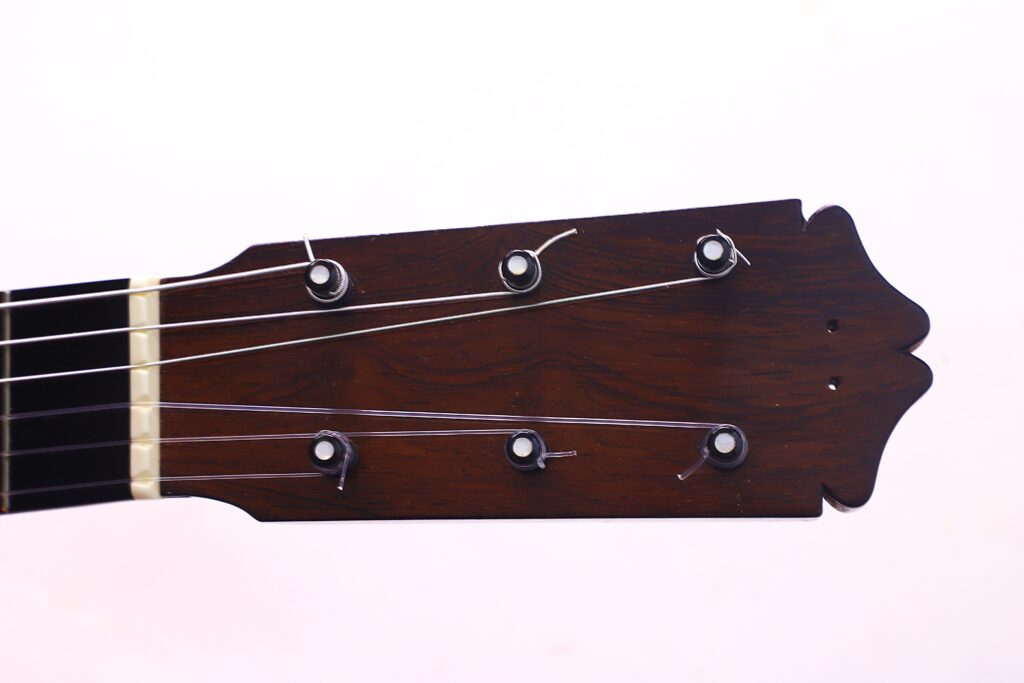 桑托斯-埃尔南德斯 1930 年弗拉门戈吉他琴头特写,深色木材、六根音栓和三根可见琴弦,背景为纯浅色。.