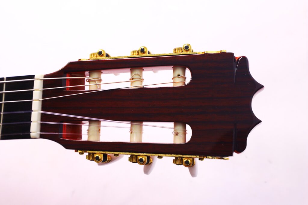 Nahaufnahme Der Kopfplatte Der Hermanos Conde 1991 Paco De Lucia Special Flamenco Gitarre, Die Nylonsaiten Und Goldene Stimmwirbel Vor Einem Schlichten, Hellrosa Hintergrund Zeigt.