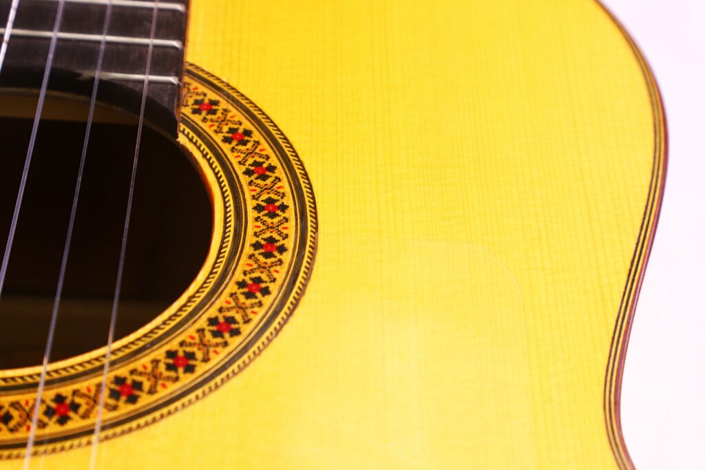 Nahaufnahme Des Korpus Der Manuel Reyes 1991 Flamenco-Gitarre, Die Das Schallloch Mit Dekorativer Rosette, Saiten Und Einem Teil Der Leuchtend Gelben Holzoberfläche Hervorhebt.
