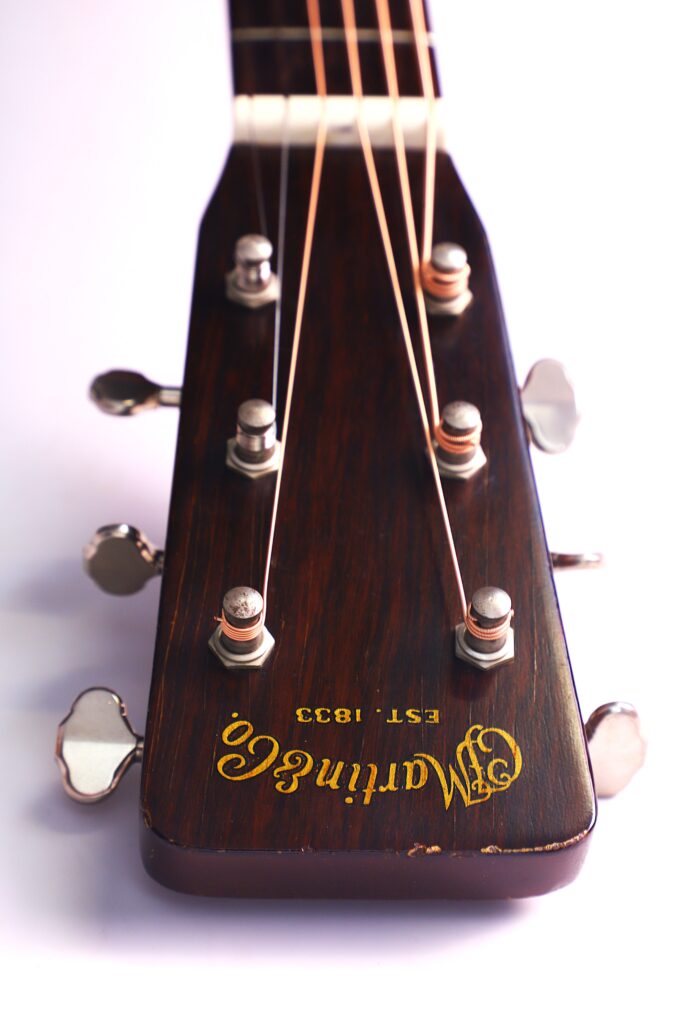 Nahaufnahme Der Kopfplatte Der Martin 000-18 1958 Akustik Gitarre, Mit Dunklem Holzfinish, Sechs Stimmwirbeln, Dem Goldenen „C.f. Martin &Amp; Co. Est. 1833“-Logo Und Fokussierten Gitarrensaiten Vor Einem Weißen Hintergrund.