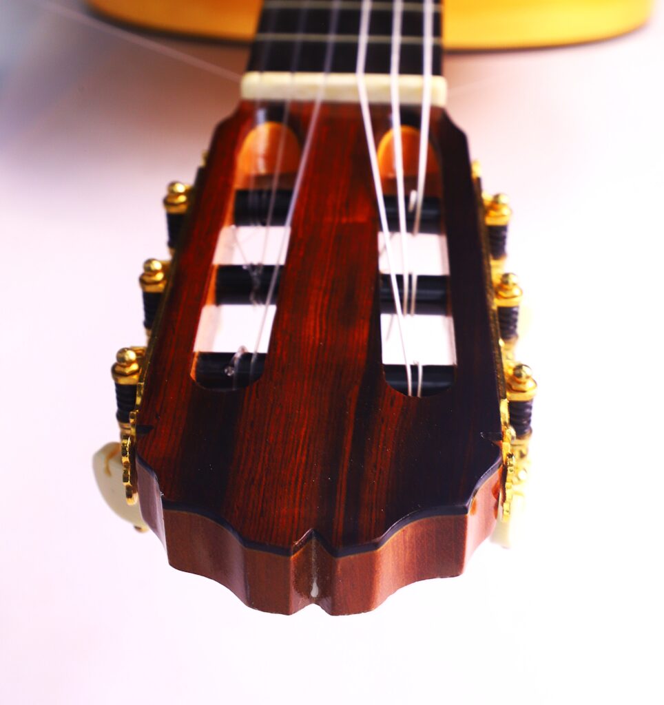 Nahaufnahme Der Kopfplatte Der Manuel Reyes Model 2021 Von Hippner Flamenco Gitarre Mit Goldenen Stimmwirbeln, Weißen Knöpfen Und Nylonsaiten, Vor Einem Hellrosa Hintergrund.