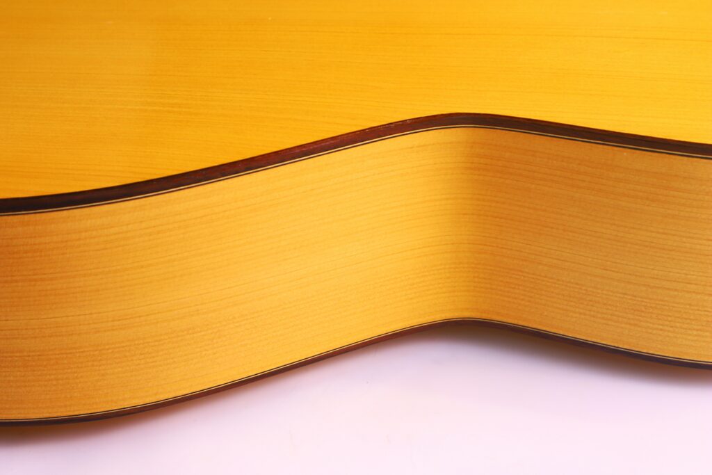 Nahaufnahme Des Korpus Der Manuel Reyes 1991 Flamenco-Gitarre, Die Die Glatte, Geschwungene Holzoberfläche Mit Einem Leicht Natürlichen Finish Und Sichtbarer Holzmaserung Hervorhebt. Das Bild Konzentriert Sich Auf Die Seitliche Und Untere Kante Der Gitarre.