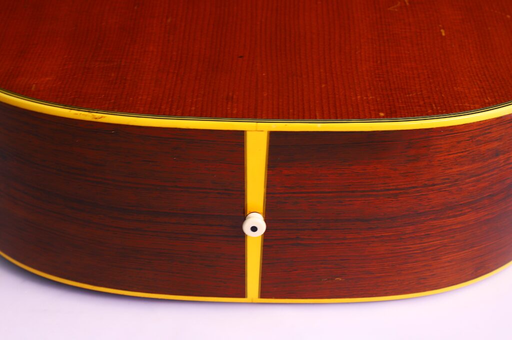 Nahaufnahme Der Unterseite Einer Martin D-28 1950 Akustik Gitarre, Die Ihren Glänzenden Holzkorpus, Die Gelbe Einfassung Und Den Mittig Platzierten Weißen Gurtknopf Hervorhebt, Alles Vor Einem Schlichten Weißen Hintergrund.