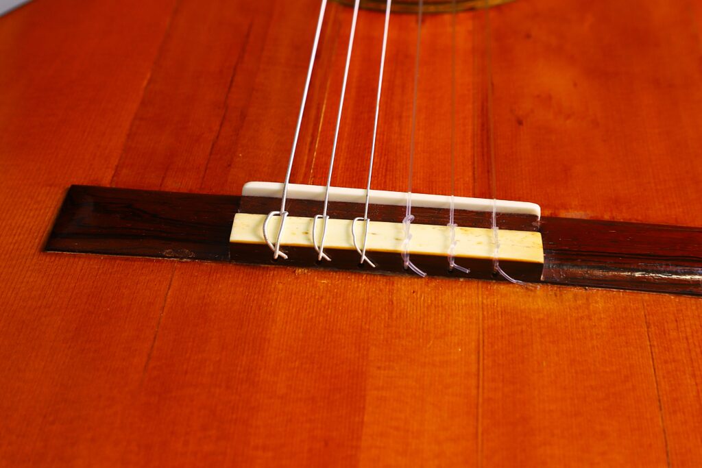 Santos Hernandez 1930 弗拉门戈吉他琴桥特写,显示五根尼龙弦连接在抛光棕色琴身上的木质琴桥上。.