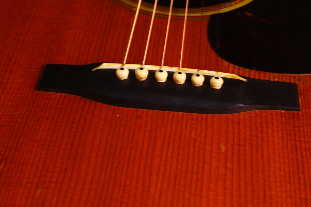 Nahaufnahme Des Stegs Und Der Saiten Der Martin D-28 1950 Akustik Gitarre Auf Einem Rötlichen Holzkorpus, Die Sechs Weiße Stegstifte, Einen Teil Des Schalllochs Und Ihre Glänzende Oberfläche Zeigt.