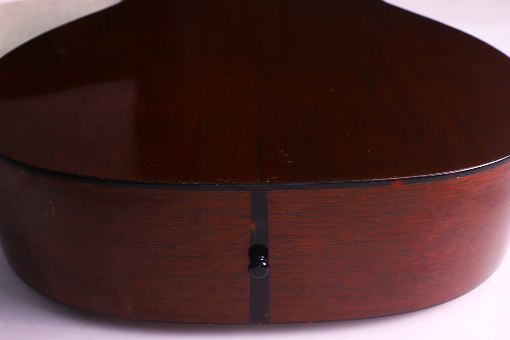 Nahaufnahme Der Rückseite Und Der Unterkante Einer Martin 000-18 1958 Akustik Gitarre, Mit Ihrer Dunkelbraunen Polierten Holzoberfläche Und Einem Schwarzen Gurtknopf In Der Mitte.