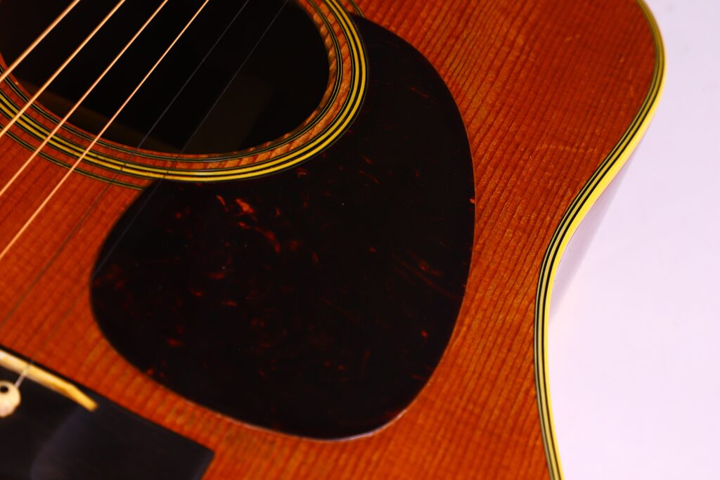 Nahaufnahme Des Korpus Einer Martin D-28 1950 Akustik Gitarre, Die Die Saiten, Das Dunkle Schlagbrett, Die Holzmaserung Und Die Gelbe Einfassung Entlang Der Kante Hervorhebt.