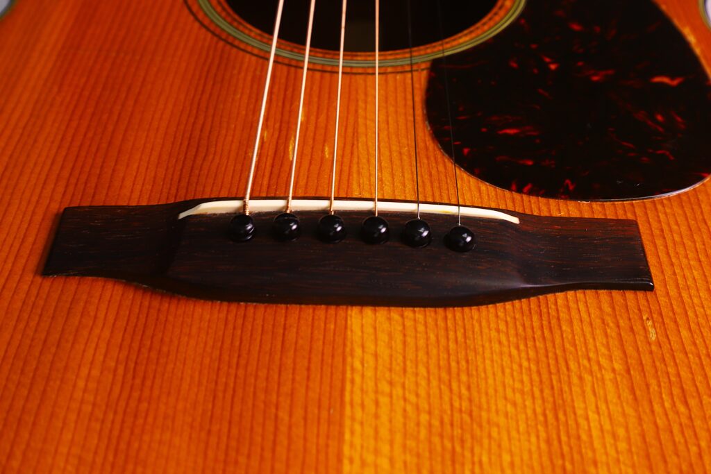 Nahaufnahme Des Stegs Und Der Saiten Der Martin 000-18 1958 Akustik Gitarre Auf Einem Holzkorpus, Die Die Feine Holzmaserung Und Die Detaillierte Handwerkskunst Am Steg Und Schlagbrett Hervorhebt.