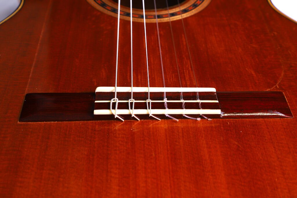 Nahaufnahme Des Stegs Und Der Saiten Der Manuel Reyes Model 2021 Von Hippner Flamenco Gitarre, Die Ihren Warmen Braunen Holzkörper Und Die Detaillierten Saitenbefestigungen Hervorhebt.