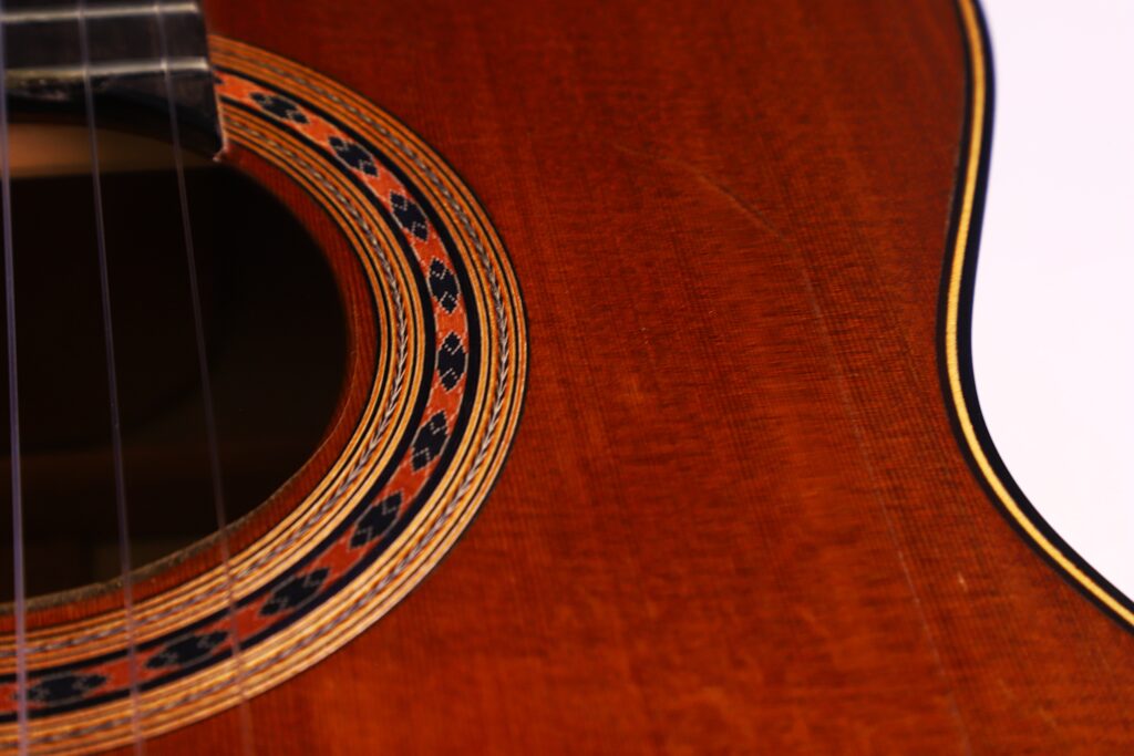 Nahaufnahme Der Manuel Reyes Model 2021 Von Hippner Flamenco Gitarre Mit Dem Schallloch, Der Dekorativen Rosette, Den Saiten Und Einem Rötlich-Braunen Holzkörper Mit Sichtbarer Maserung.