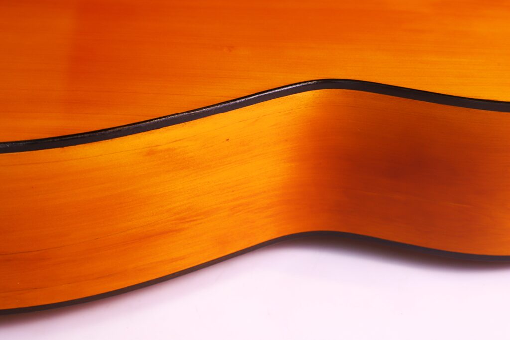 Santos Hernandez 1930 弗拉门戈吉他侧面特写,显示其光滑、抛光的橙棕色木质和白色背景下优雅的黑色边缘。.