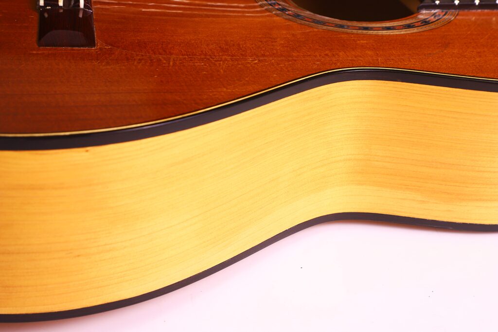 Nahaufnahme Der Manuel Reyes Model 2021 Von Hippner Flamenco Gitarre, Die Ihre Holzmaserung An Der Seite Und Am Unteren Korpus Mit Kontrastierenden Dunklen Und Hellen Tönen Hervorhebt; Ein Teil Des Schalllochs Ist Oben Rechts Sichtbar.