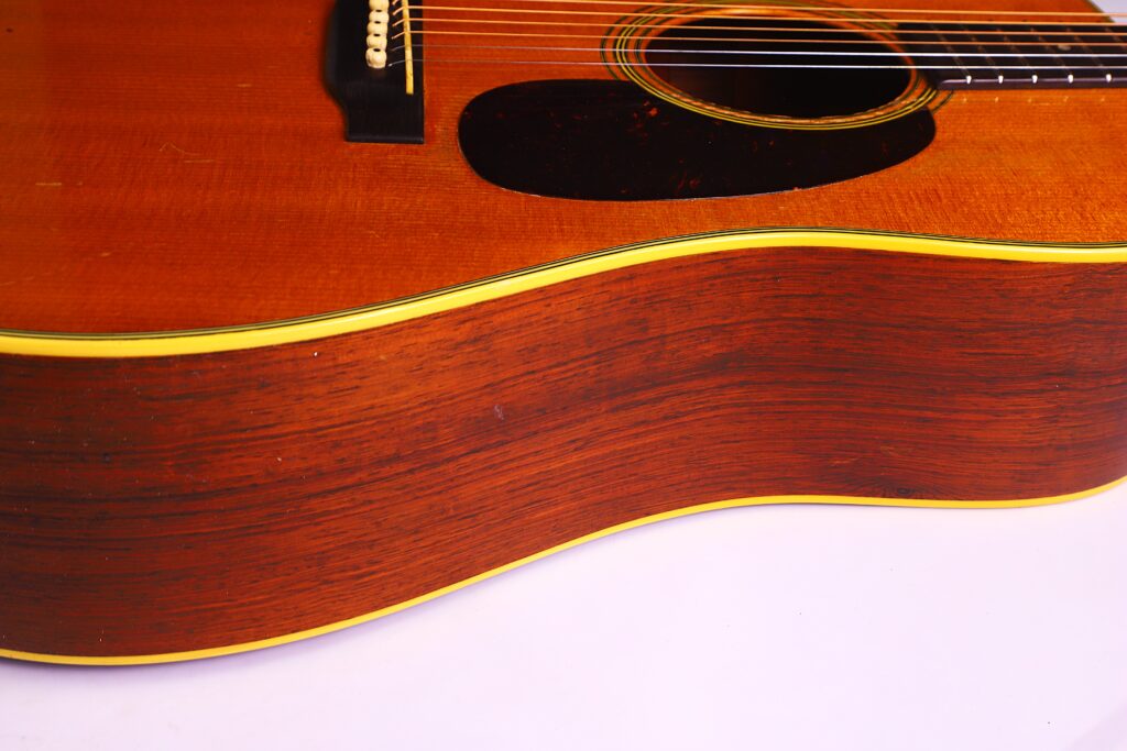 Seitenansicht In Nahaufnahme Einer Martin D-28 1950 Akustik Gitarre, Die Ihren Glänzenden Holzkorpus, Die Gelbe Kantenbindung Und Einen Teil Der Saiten Und Des Stegs, Die Oben Sichtbar Sind, Hervorhebt.