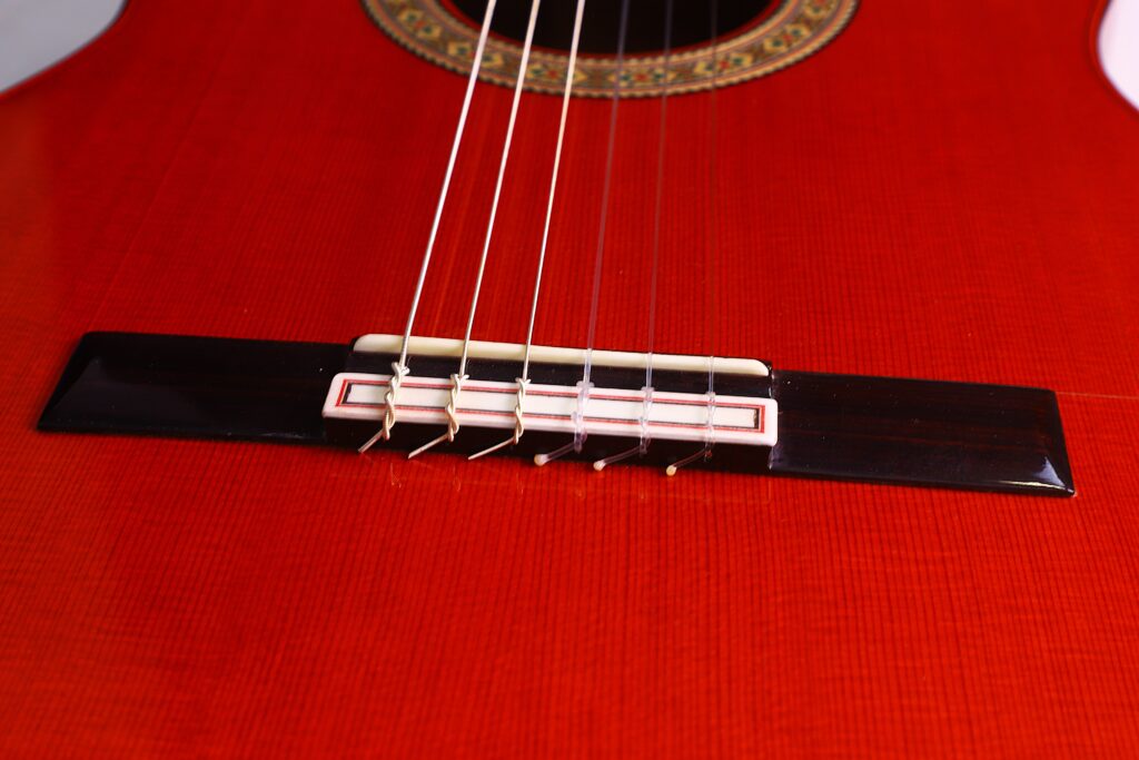 Nahaufnahme Des Stegs Und Der Saiten Der Hermanos Conde 1991 Paco De Lucia Special Flamenco Gitarre Mit Glänzend Roter Oberfläche, Feiner Holzmaserung Und Dekorativer Rosette Am Schallloch.