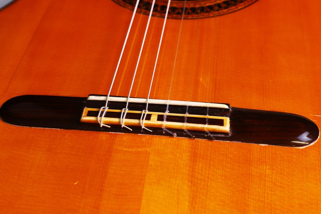 Nahaufnahme Des Stegs Und Der Saiten Einer Luis Sanchez 2011 Negra Flamenco Gitarre, Die Den Glänzenden Holzkörper, Den Detaillierten Sattel Und Die Saitenknoten Hervorhebt.