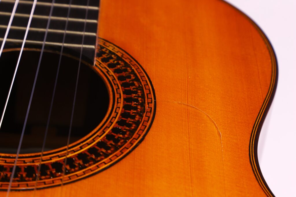 Nahaufnahme Einer Luis Sanchez 2011 Negra Flamenco Gitarre, Die Ihre Saiten, Einen Teil Des Dekorativen Schalllochs Und Einen Sichtbaren Kratzer Auf Dem Holzkörper Zeigt.