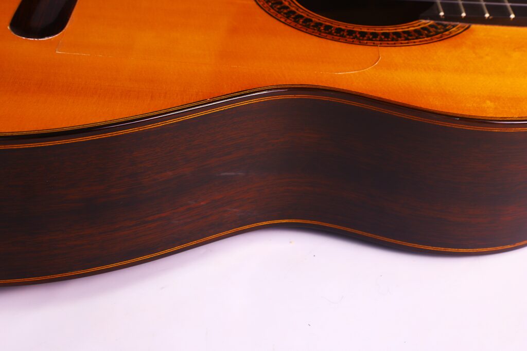 Nahaufnahme Der Seite Und Eines Teils Der Decke Einer Luis Sanchez 2011 Negra Flamenco Gitarre, Die Ihre Holzmaserung Und Die Detaillierte Handwerkskunst Vor Einem Weißen Hintergrund Zeigt.