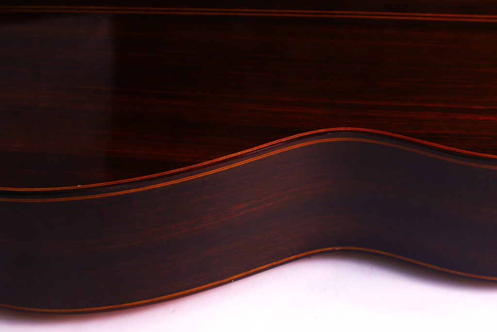 Nahaufnahme Der Dunklen Holzseite Einer Luis Sanchez 2011 Negra Flamenco Gitarre Mit Einer Glatten, Wellenförmigen Kontur Vor Einem Weißen Hintergrund. Die Holzmaserung Und Die Geschichtete Kante Der Gitarre Sind Deutlich Sichtbar.