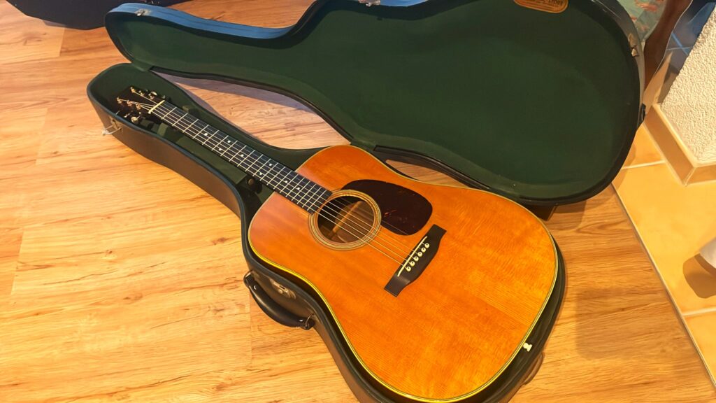 Eine Martin D-28 1950 Akustik Gitarre Mit Natürlicher Holzoberfläche Liegt In Einem Offenen, Grün Ausgekleideten Hartschalenkoffer Auf Einem Holzboden.