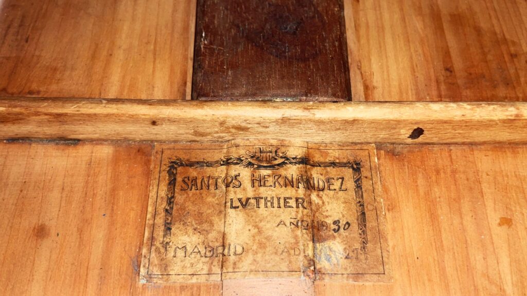 特写显示了 Santos Hernandez 1930 弗拉门戈吉他内部的标签,上面刻有 „Santos Hernandez Luthier Ano 1930 Madrid “字样,表明了木质内部的制造商和年份。.