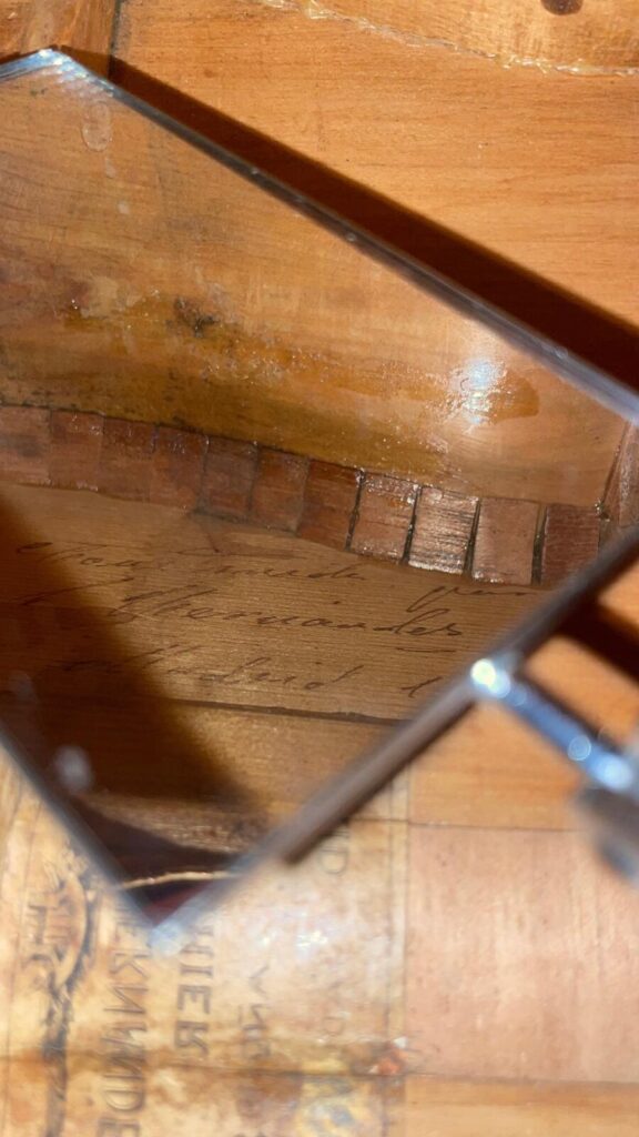 一张特写照片展示了木头上的放大镜,显示出手写的草书文字,就像桑托斯-埃尔南德斯 1930 年弗拉门戈吉他上的标记。背景模糊不清,突出了放大的文字。.