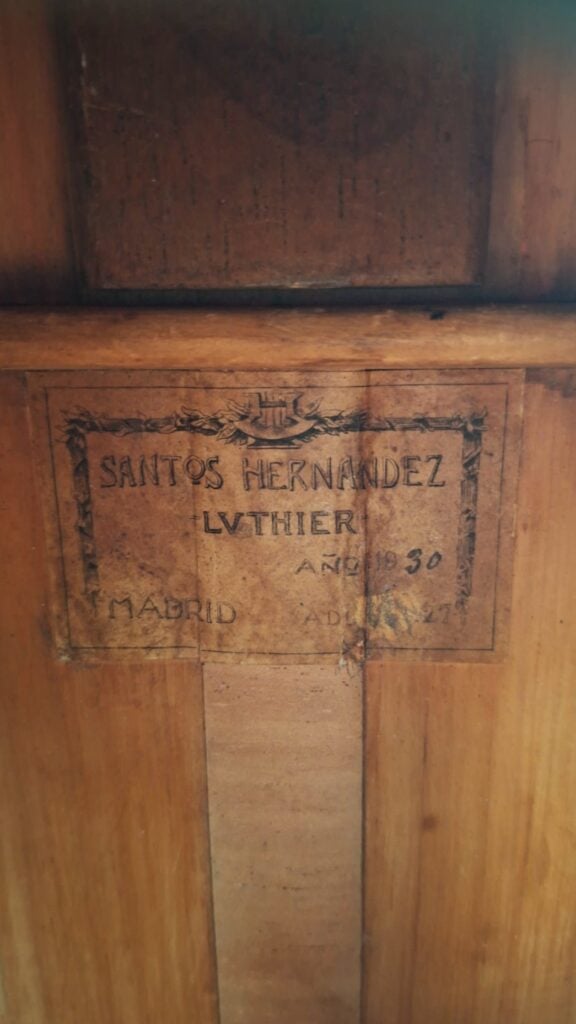 Auf einer Nahaufnahme eines Holzschilds im Inneren des Instruments ist zu lesen: „Santos Hernandez, Luthier, Ano 1930, Madrid“ – was bestätigt, dass es sich hierbei um die Santos-Hernandez-Flamenco-Gitarre von 1930 handelt. Auf einer Nahaufnahme eines Holzschilds im Inneren des Instruments ist zu lesen: „Santos Hernandez, Luthier, Ano 1930, Madrid“ – was bestätigt, dass es sich hierbei um die Santos-Hernandez-Flamenco-Gitarre von 1930 handelt.