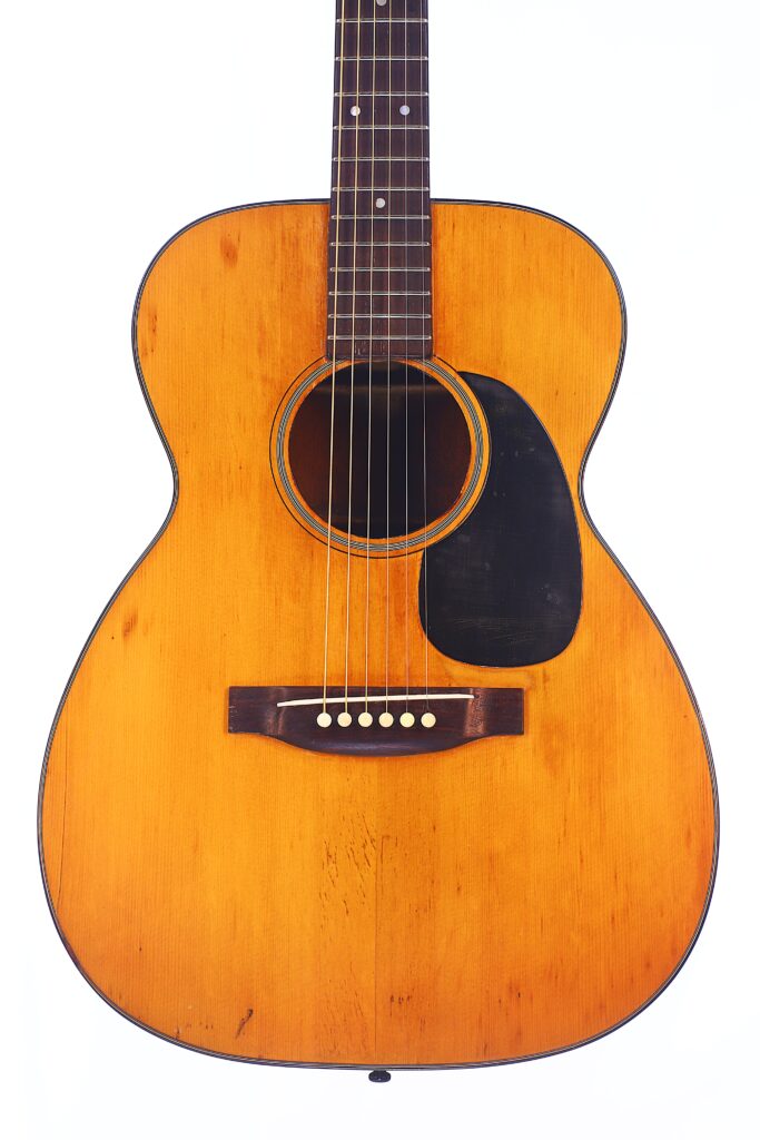 A Martin 00-18 1946 Acoustic Guitar With A Natural Wood Finish, Visible Grain Patterns, Black Pickguard, And Six Strings Is Photographed Upright Against A White Background.