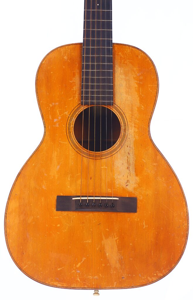 A Close-Up Of A Martin 0-18 1926 Acoustic Guitar With A Worn, Orange-Brown Wooden Body, Six Strings, And Visible Scratches, Showing Signs Of Frequent Use Against A White Background.