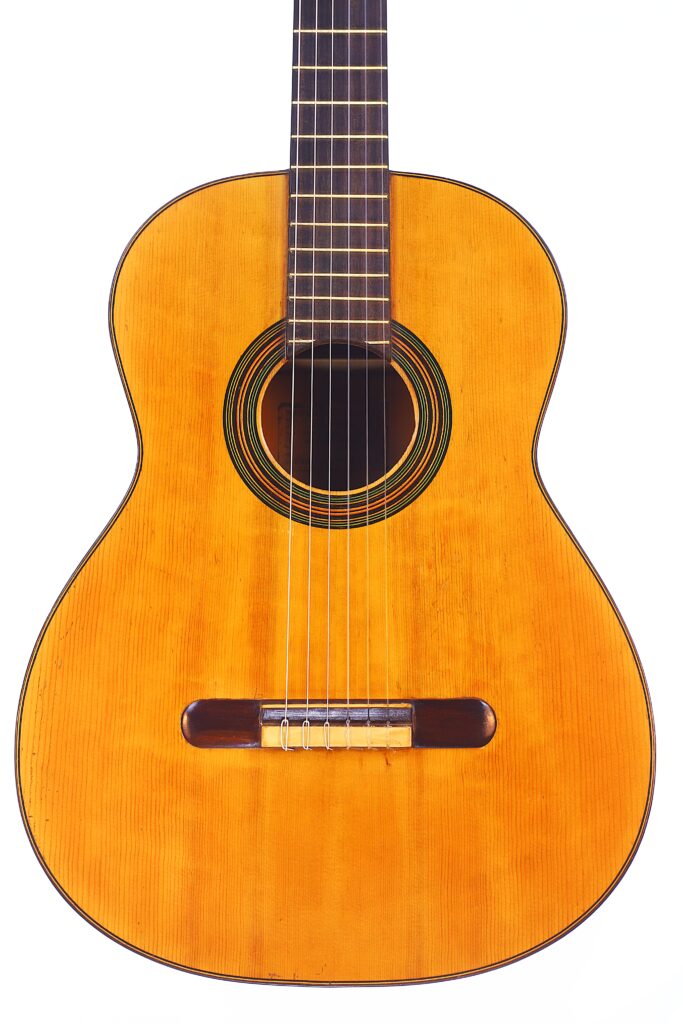 A guitarra clássica Domingo Esteso 1934 apresenta um corpo em madeira, seis cordas, um orifício de som redondo com anéis decorativos e uma escala escura, retratada contra um fundo branco.