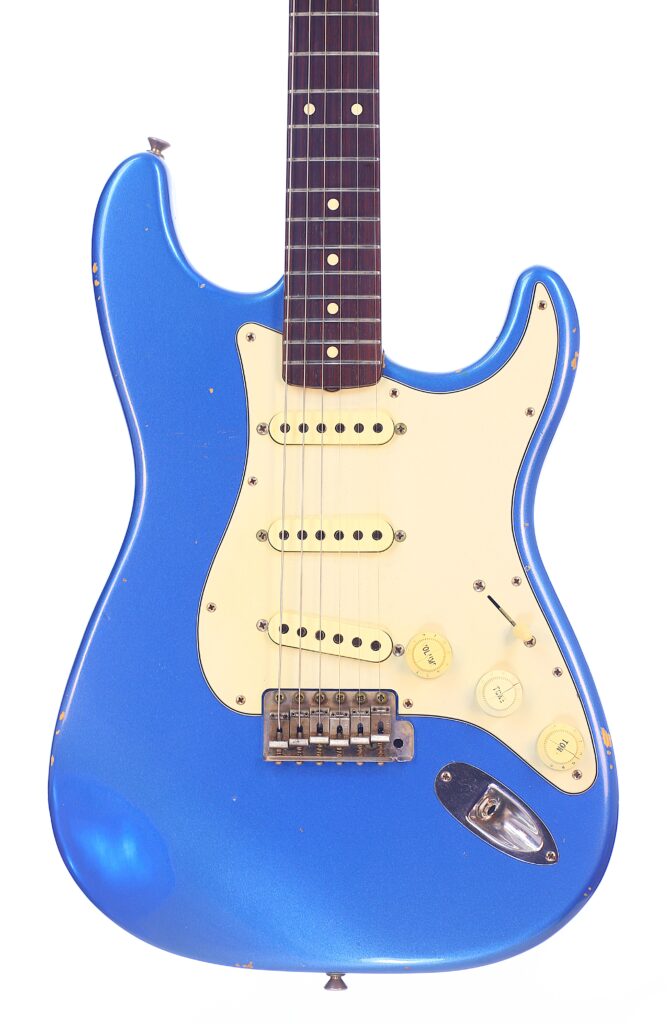 Eine Nahaufnahme Der Blauen Fender Stratocaster 1960 Relic Cunetto/Cruz E-Gitarre, Die Ein Cremefarbenes Schlagbrett, Drei Single-Coil-Tonabnehmer, Gelbe Regler, Leichte Gebrauchsspuren Am Korpus Und Einen Weißen Hintergrund Zeigt.