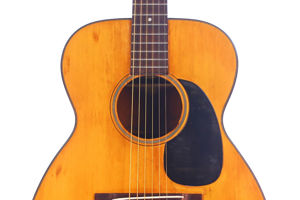A Close-Up Of The Martin 00-18 1946 Acoustic Guitar Displays Its Body, Sound Hole, Strings, And Black Pickguard With A Natural Wood Finish Set Against A White Background.