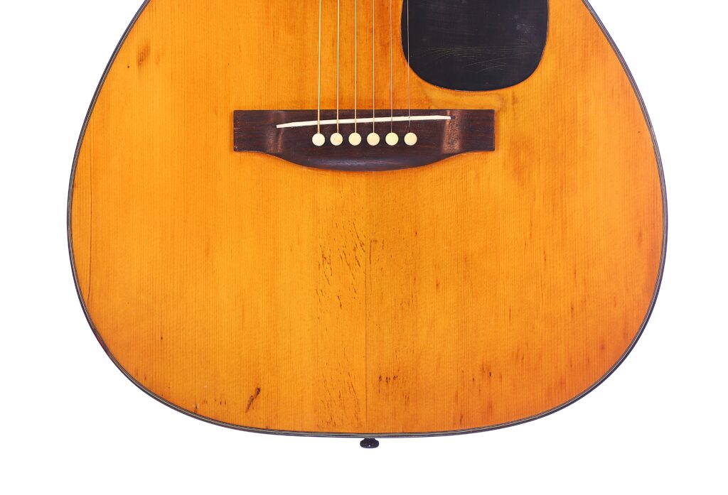 Close-Up Of The Martin 00-18 1946 Acoustic Guitar Body, Featuring Six Strings, A Wooden Bridge With Six White Pins, A Black Pickguard, And A Natural Wood Finish.