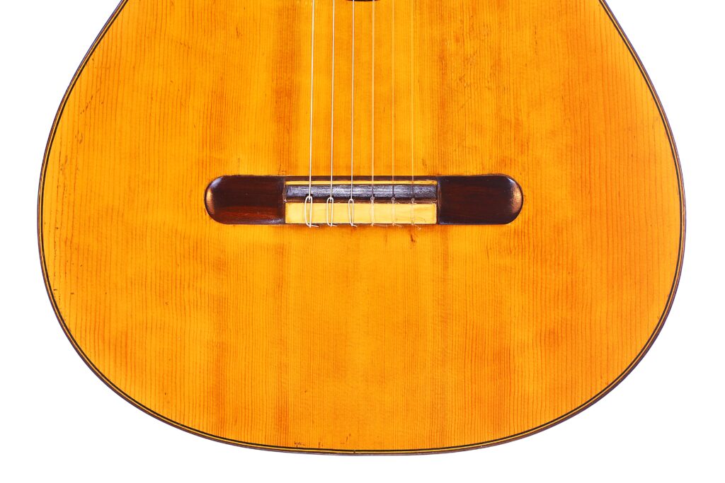 Grande plano do corpo da guitarra clássica Domingo Esteso 1934, destacando as cordas, o cavalete e o grão de madeira natural contra um fundo branco.