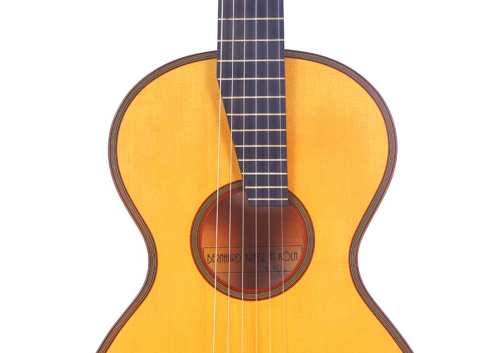 A Close-Up Of The Bernhard Kresse 2011 Stauffer Romantic Guitar'S Body And Neck, Displaying Six Strings, A Wooden Soundboard, And A Round Sound Hole Against A White Background.
